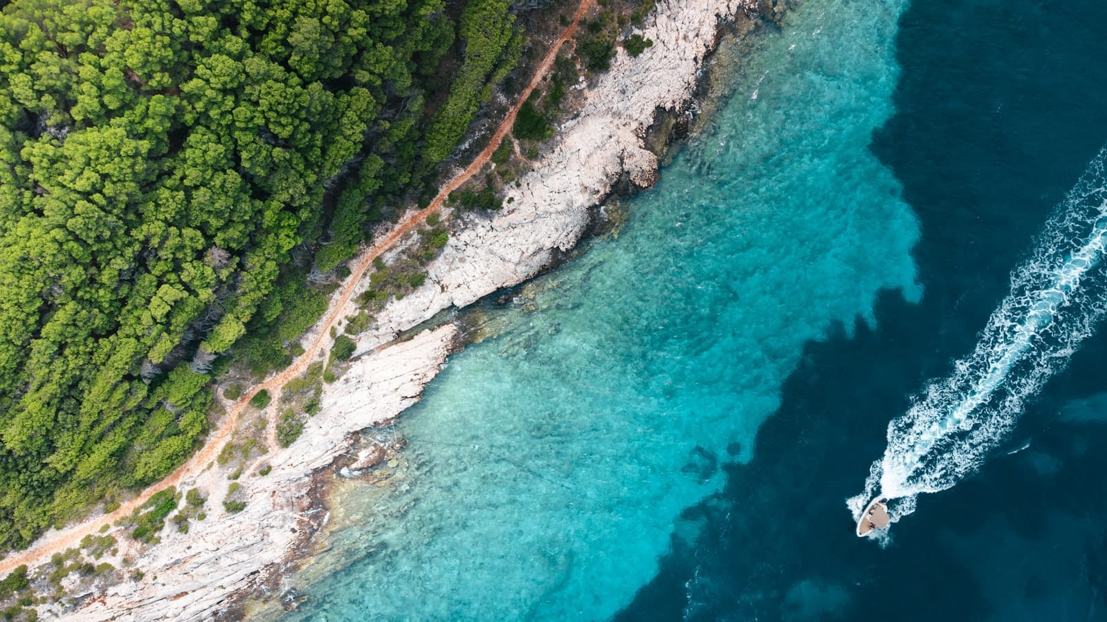 Vista aérea de uma lancha percorrendo o litoral turquesa de uma exuberante ilha dálmata na Croácia.