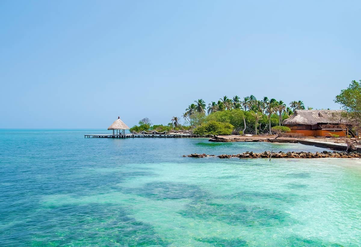 Clear turquoise water and a thatched-roof pier on a palm-fringed island in Islas del Rosario National Park near Cartagena, Colombia.