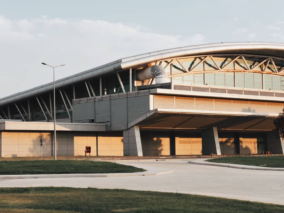 Modernes Außengebäude des Terminals des Flughafens Sabiha Gökçen mit geschwungenem Dach, Glasfenstern und Straße im Vordergrund an einem klaren Tag.