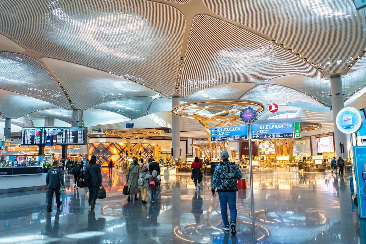 Geräumiges, modernes Terminalinneres des Istanbul Airport mit Passagieren, Beschilderung, Sitzgelegenheiten und gut beleuchteten architektonischen Deckendetails.
