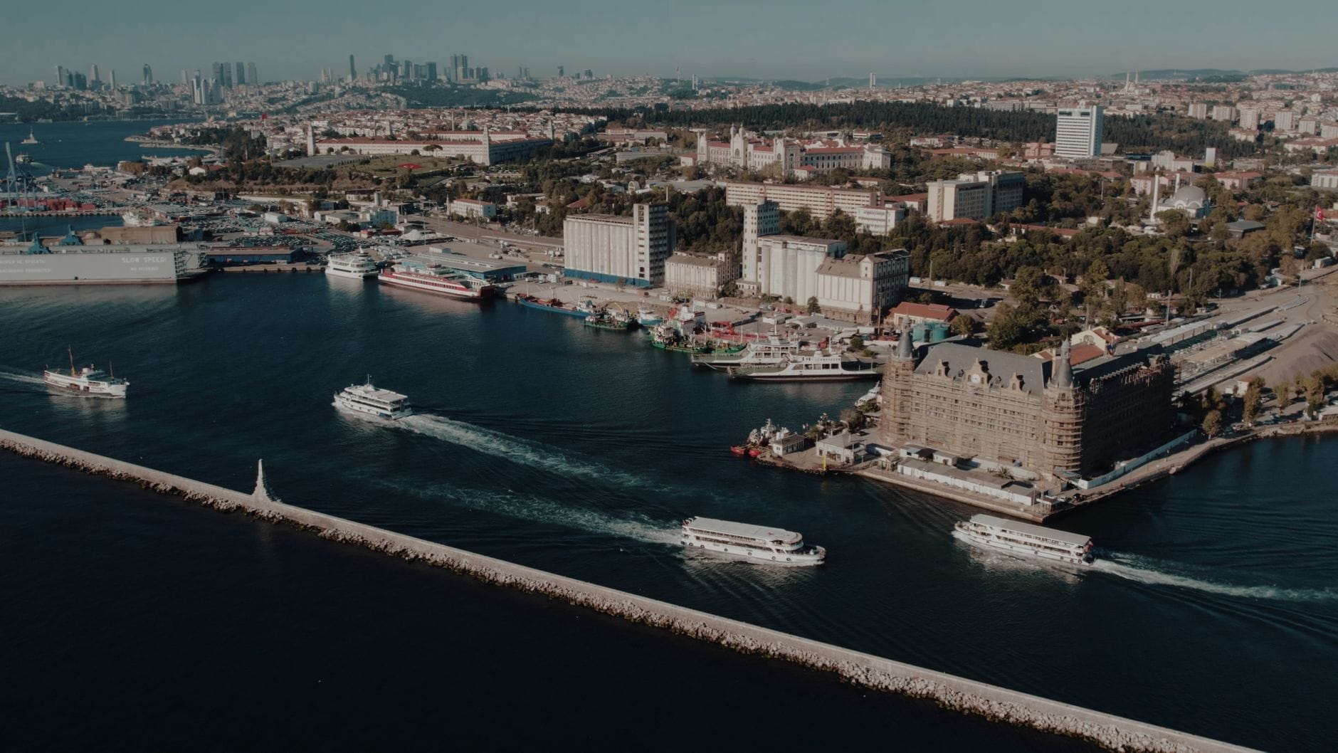 Vista aérea do orla de Kadıköy com balsas cruzando o Bósforo, a histórica Estação Ferroviária de Haydarpaşa e o skyline do lado asiático de Istambul ao fundo.
