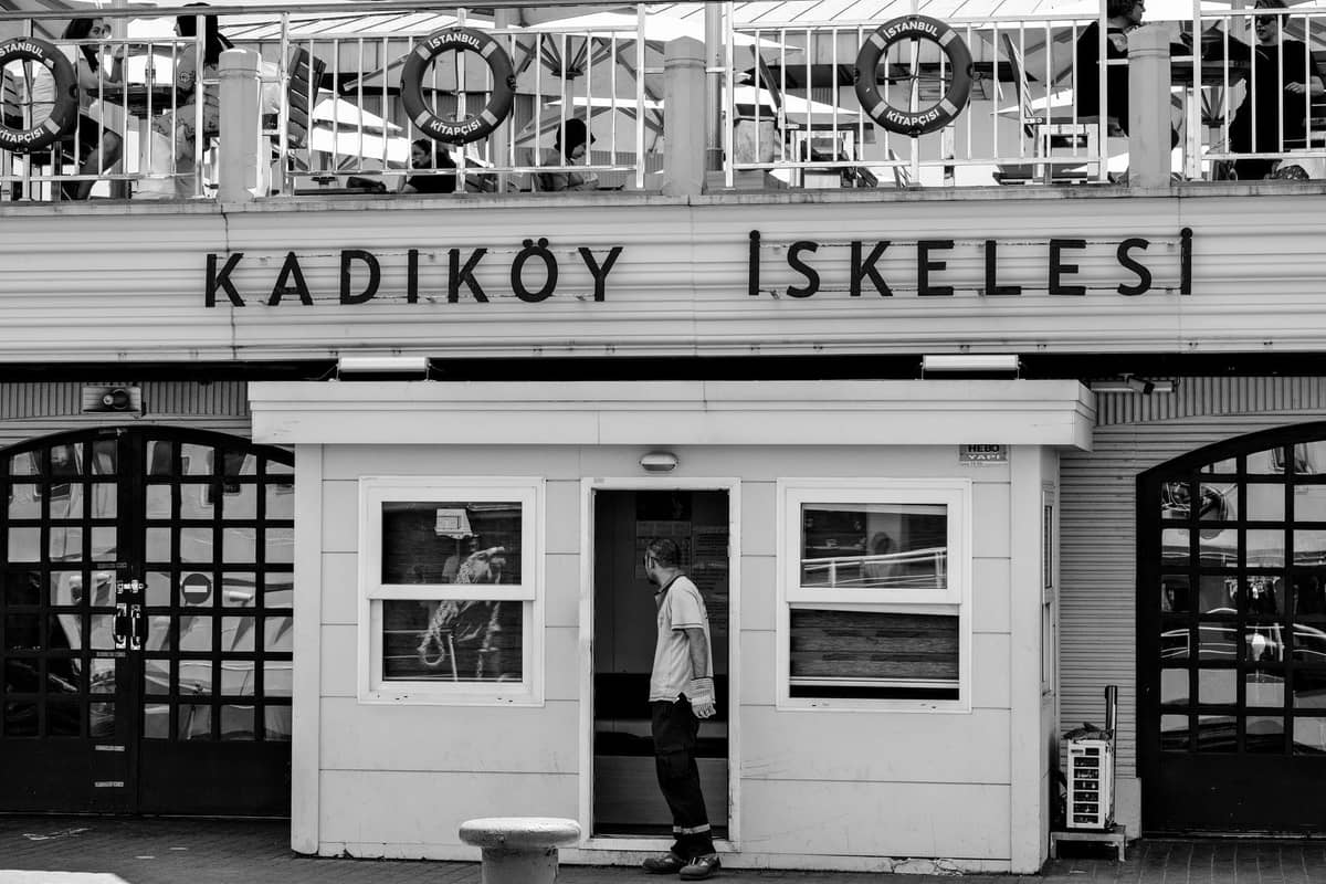 Чёрно-белая фотография главного фасада паромного терминала Kadıköy с чёткими указателями и человеком, входящим в здание.