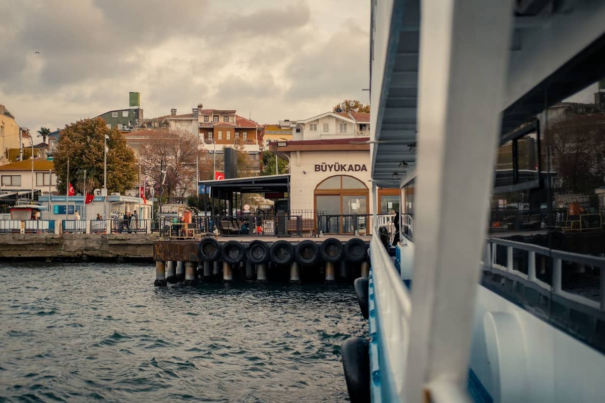 Büyükada iskelesine yanaşan feribot, yamaçtaki evler ve feribot terminaliyle birlikte Adalar'a varış sahnesini gözler önüne seriyor.