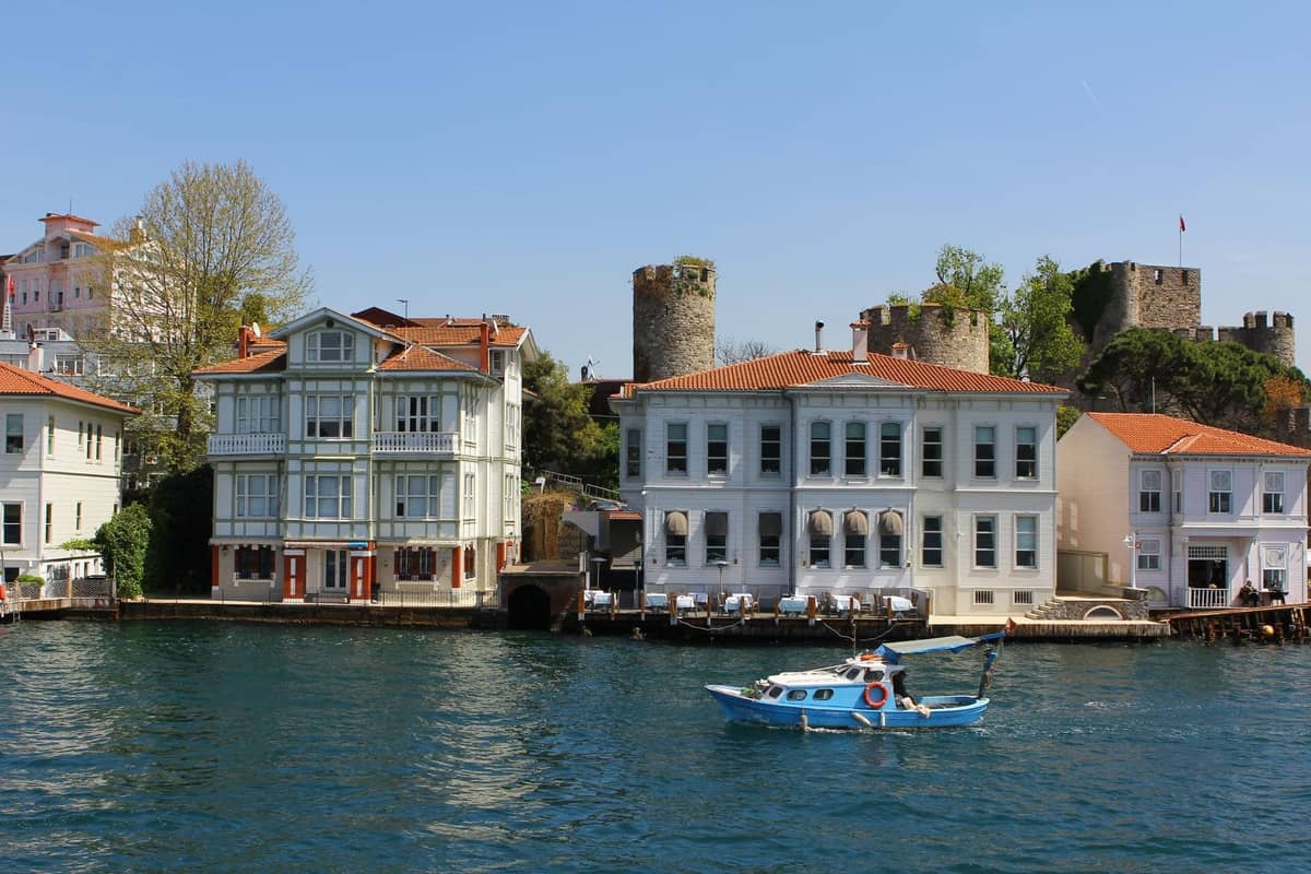 İstanbul'da Boğaz kıyısındaki bir köyde kırmızı kiremitli çatılara, taş kulelere ve bir tekneye sahip geleneksel kıyı evleri.