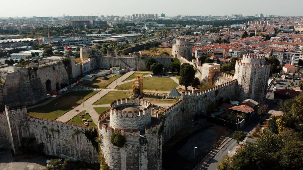 Widok z lotu ptaka na masywne Mury Teodozjańskie w Stambule, ukazujący solidne kamienne wieże, blanki i panoramę miasta w tle.
