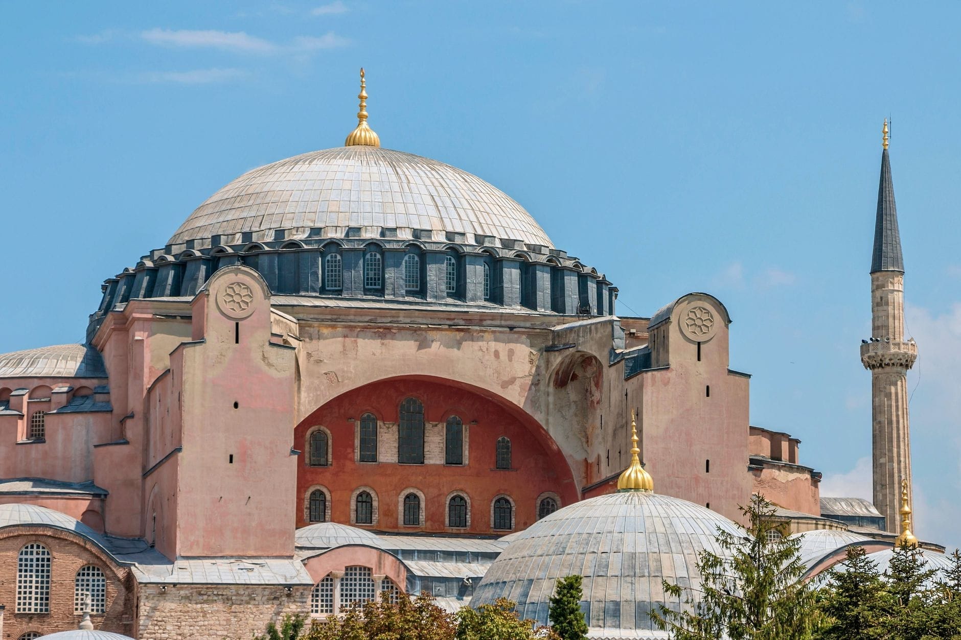 Vista exterior da Hagia Sophia em Istambul sob um céu azul intenso, destacando sua imensa cúpula, minaretes e arquitetura bizantina.