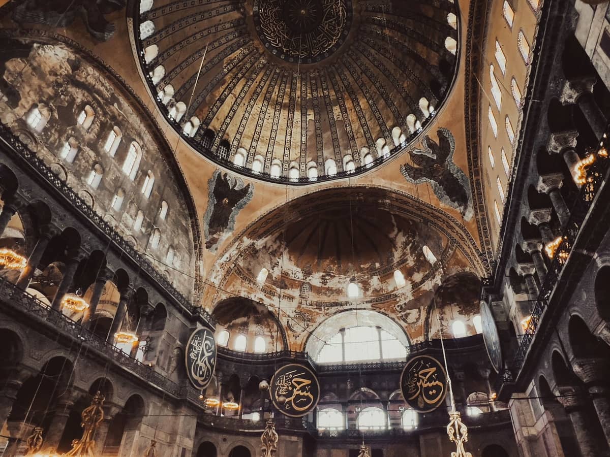 Szeroki widok wnętrza Hagia Sophia ukazujący wspaniałe kopuły, mozaiki bizantyjskie, islamską kaligrafię i okna łukowe z wpadającym naturalnym światłem.