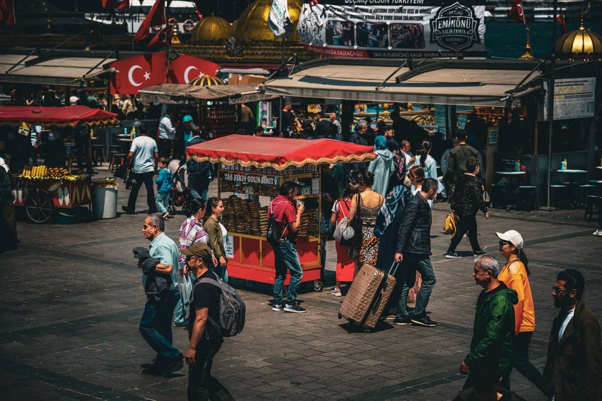 Belebter Straßenmarkt in Istanbul mit türkischen Essensständen, roten Karren, türkischen Flaggen und Passanten, der das kulinarische Straßenleben einfängt.