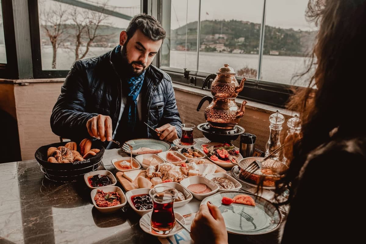 Traditionelles türkisches Frühstück mit Tee in Tulpengläsern und einem Samowar, an einem Fenster mit Blick auf den Bosporus in Istanbul.
