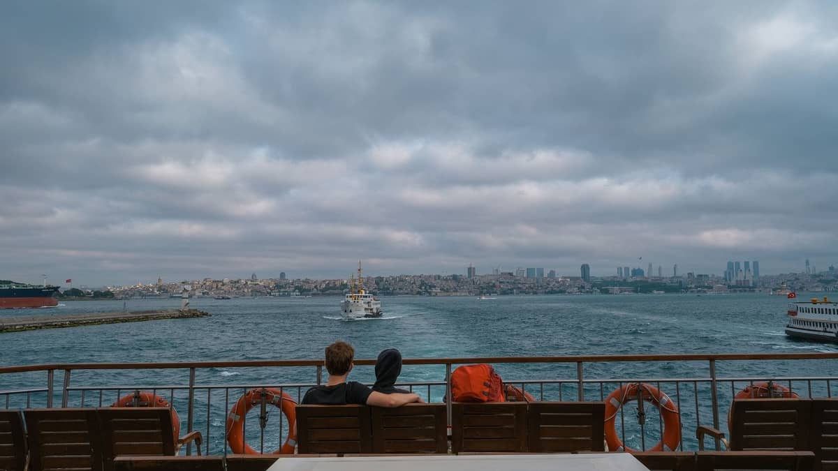 Paar, das eng beieinander auf einer Fähre sitzt, mit Blick auf die Ufersilhouette von Istanbul und anderen Fähren auf dem Bosporus.