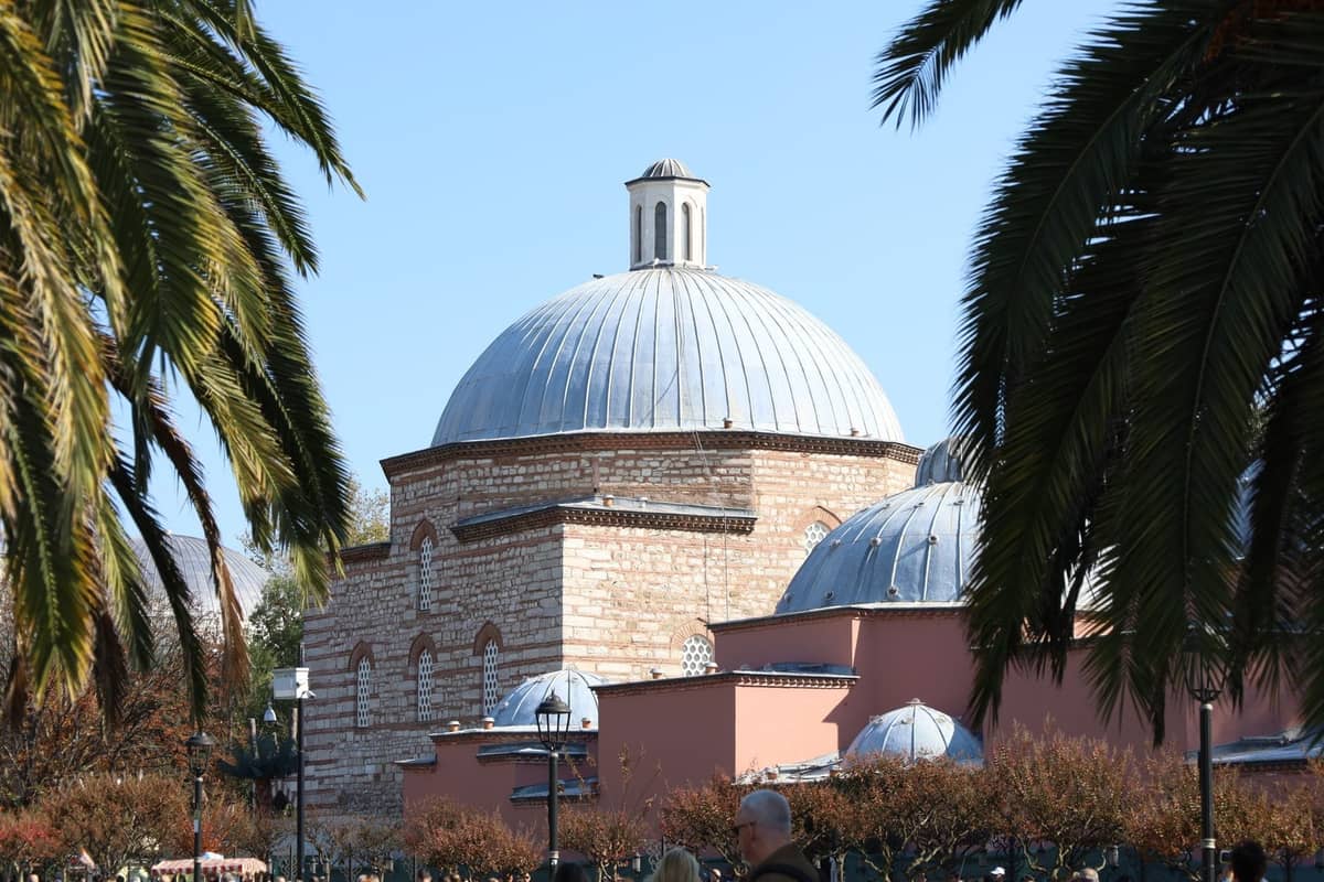 Historisches Kuppelgebäude eines türkischen Hamams in Istanbul, umgeben von Palmen und klarem Himmel.