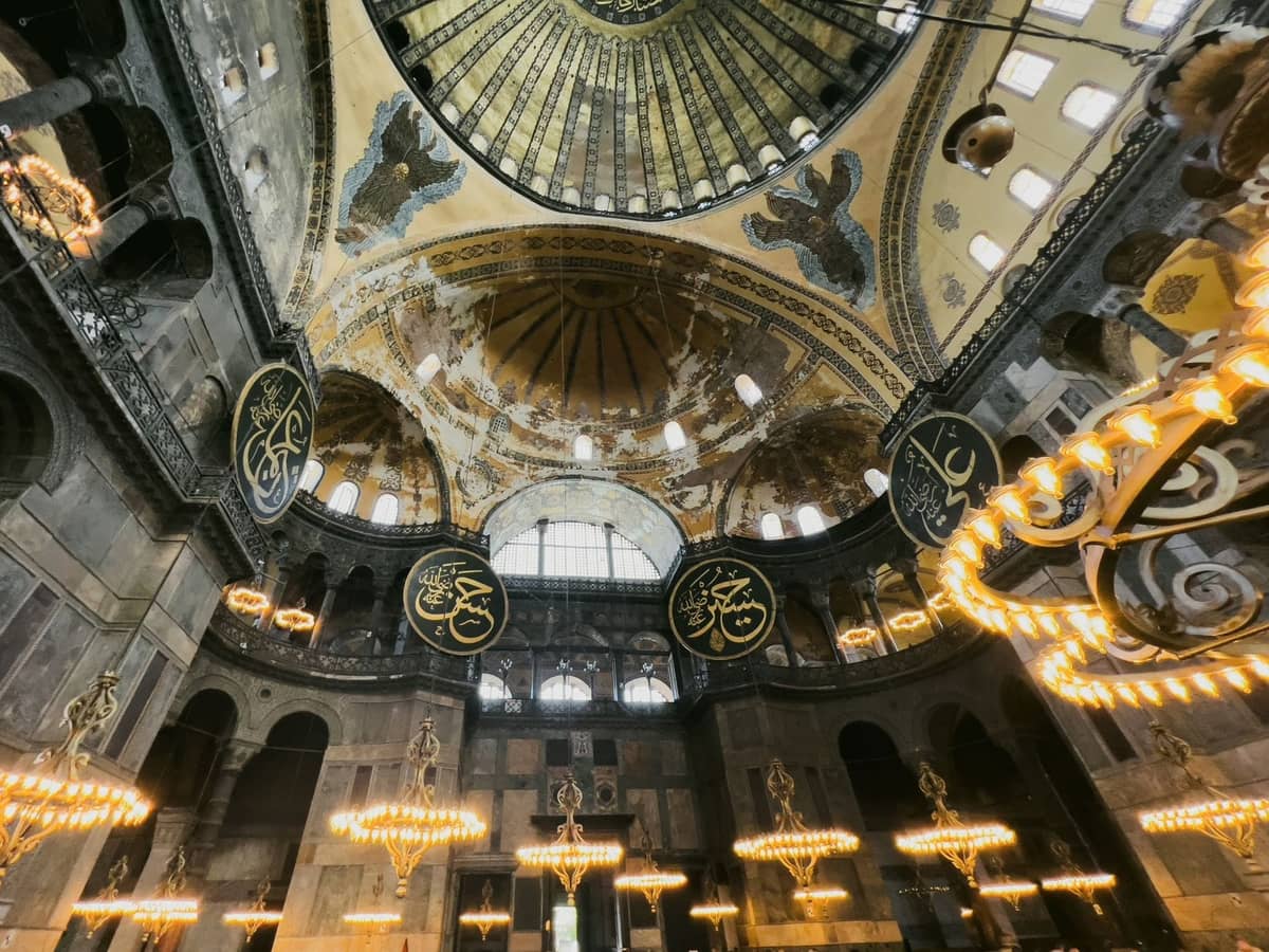 Widok wnętrza Hagia Sophia z ozdobnymi kopułami, żyrandolami, ogromnymi łukami i dużymi kaligraficznymi medalionami w Stambule.
