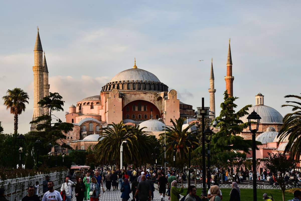 Tłumy ludzi spacerują i rozmawiają w pobliżu Hagia Sophia w Stambule, a w tle widać zieleń i historyczny budynek z kopułą.
