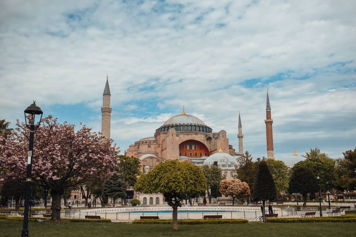 Hagia Sophia mit blühenden Frühlingsbäumen und spazierenden Menschen im Vordergrund an einem bewölkten Tag in Istanbul.