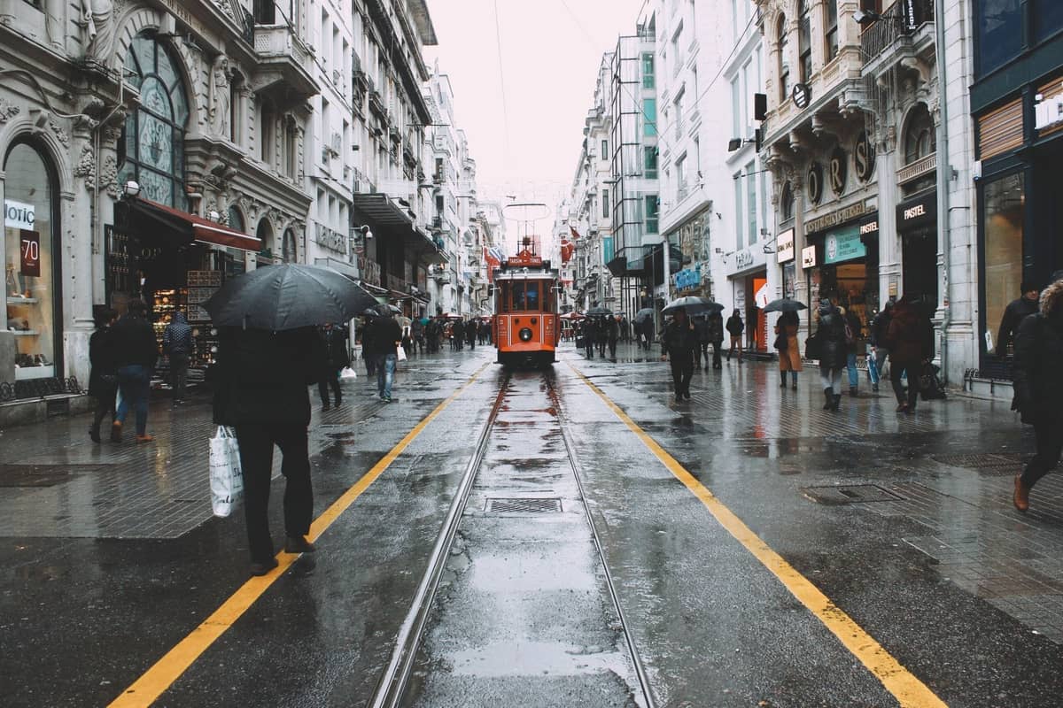Menschen mit Regenschirmen auf der nassen İstiklal Avenue in Istanbul, mit der ikonischen roten Straßenbahn im Zentrum der regnerischen Straße.