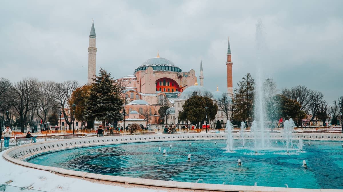 Kış mevsiminde Ayasofya, yerde kar, ön planda büyük bir çeşme ve İstanbul üzerinde bulutlu gökyüzü.