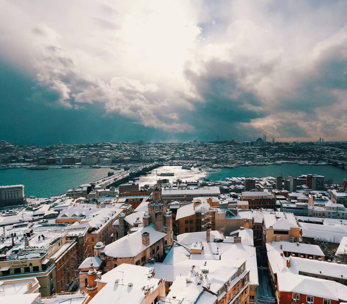 İstanbul'un karlı çatıları ve Haliç üzerindeki dramatik bulutlarıyla panoramik kış manzarası, gerçekçi bir soğuk hava sahnesini gösteriyor.