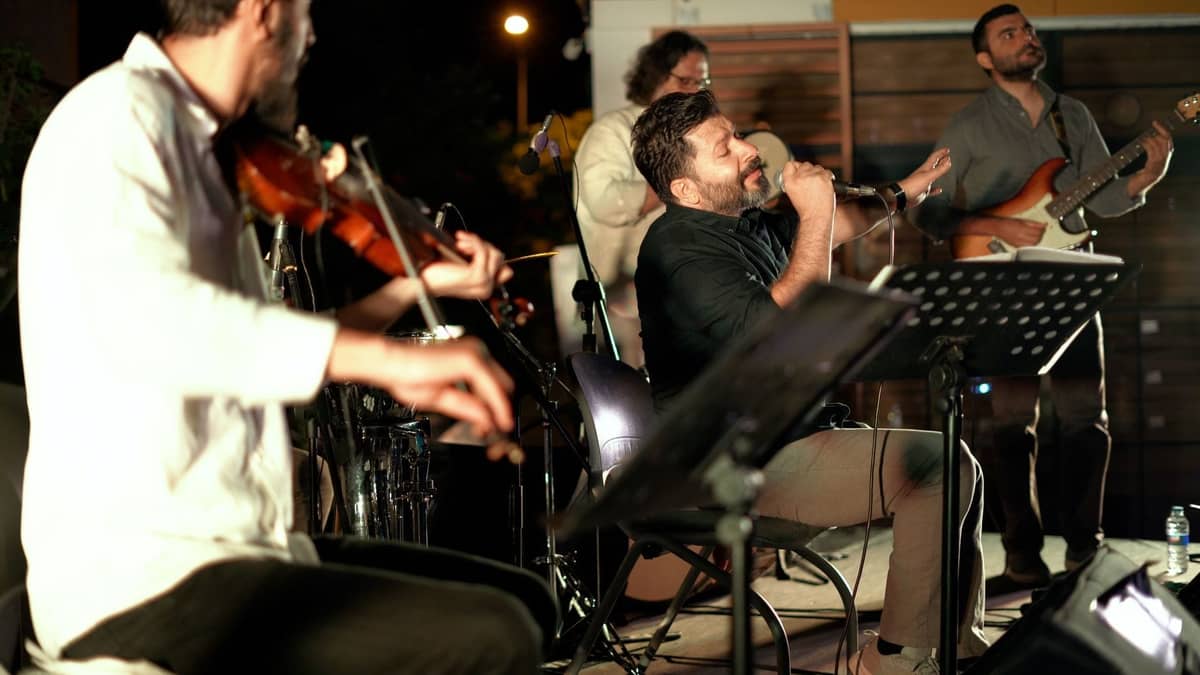 Ein kleines Musikensemble mit Geige, Gitarre, Schlagzeug und Sänger tritt in einem Innenraum auf und beschwört die lebhafte Atmosphäre einer traditionellen türkischen Meyhane-Nacht.