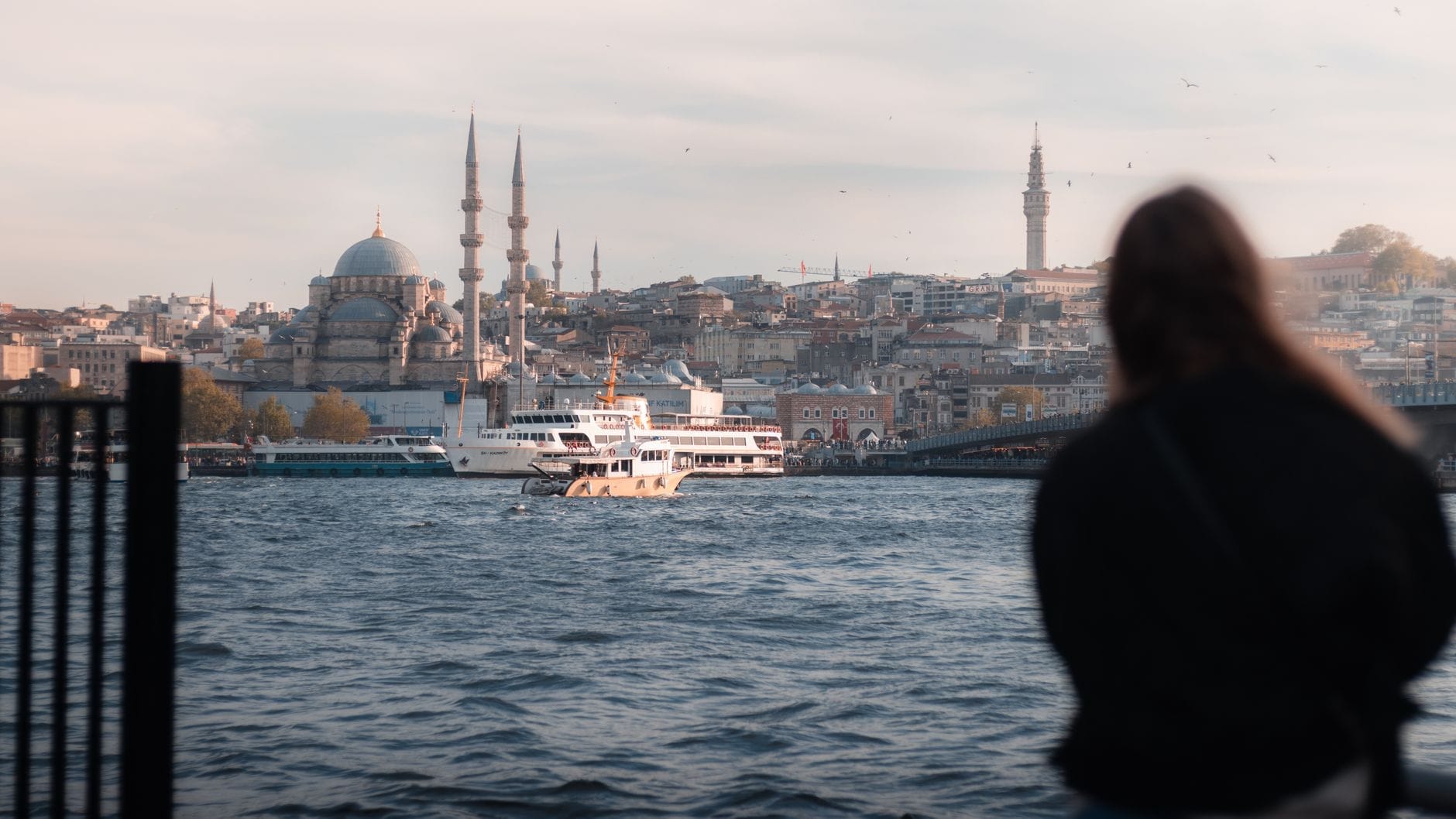 Viajantes contemplam o Bósforo com o skyline de Istambul ao fundo — mesquitas, minaretes e balsas compondo uma cena vibrante e cheia de charme histórico ao pôr do sol.