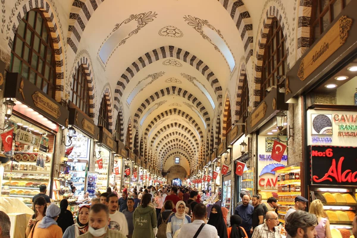 Belebtes Inneres des Gewürzbasars in Istanbul mit Gewölbedecke, türkischen Flaggen und Menschenmengen, die an Ständen mit Gewürzen und Süßigkeiten stöbern.