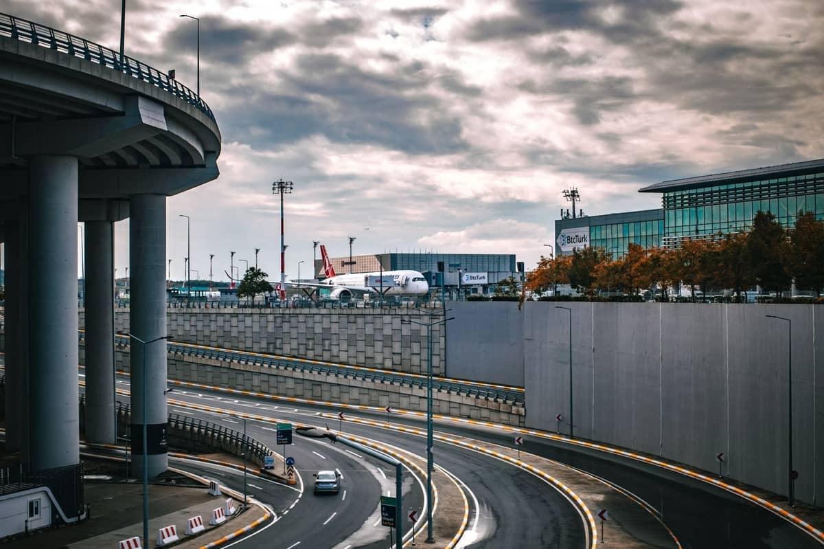 Geschwungene Zufahrtsstraßen zum Flughafen mit Überführung, Terminalgebäude und Turkish Airlines-Flugzeug am Flughafen Istanbul unter bewölktem Himmel.