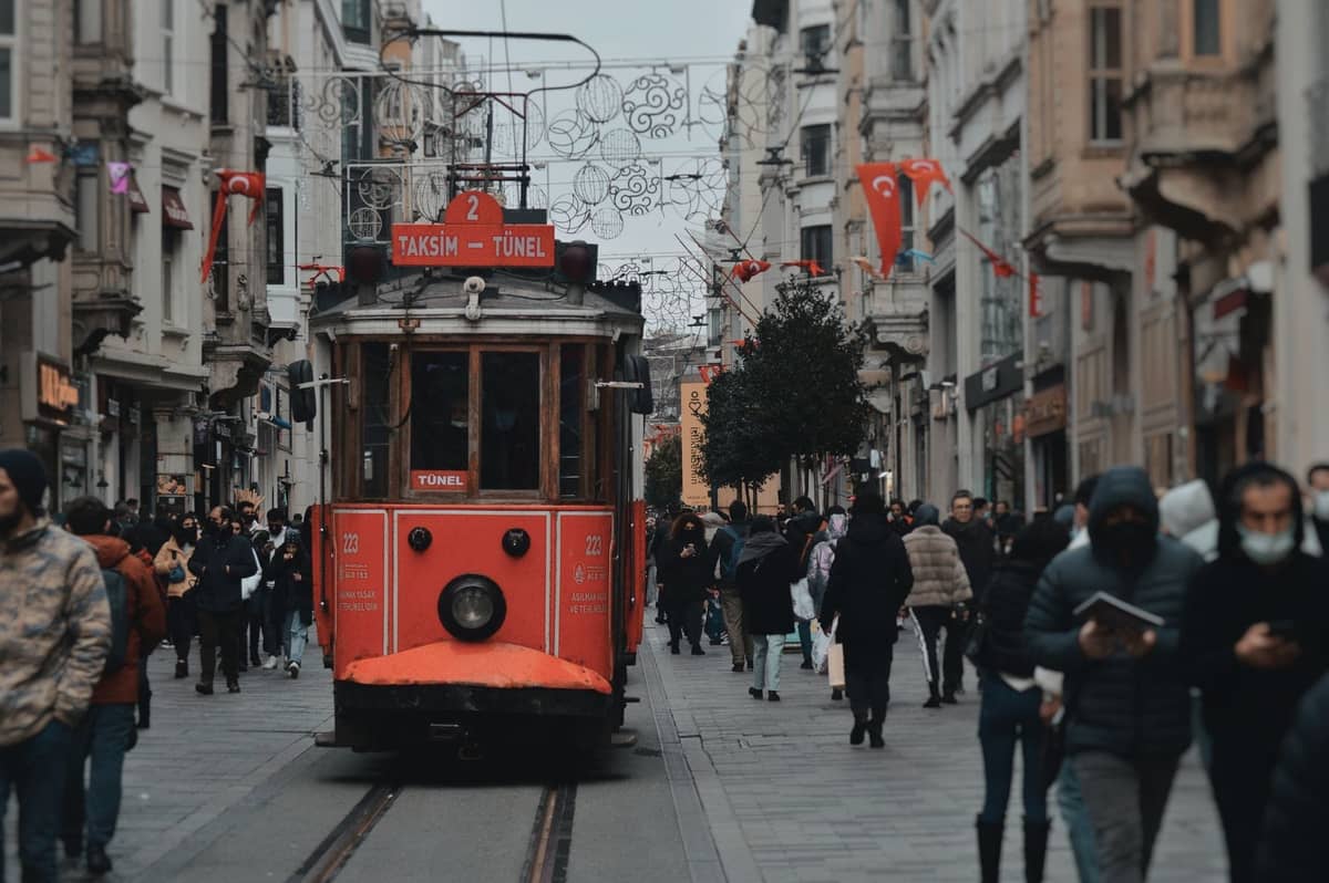 Die ikonische rote Straßenbahn Taksim-Tünel fährt die belebte İstiklal Avenue in Beyoğlu, Istanbul, entlang, umgeben von Fußgängern und historischen Gebäuden aus dem 19. Jahrhundert.
