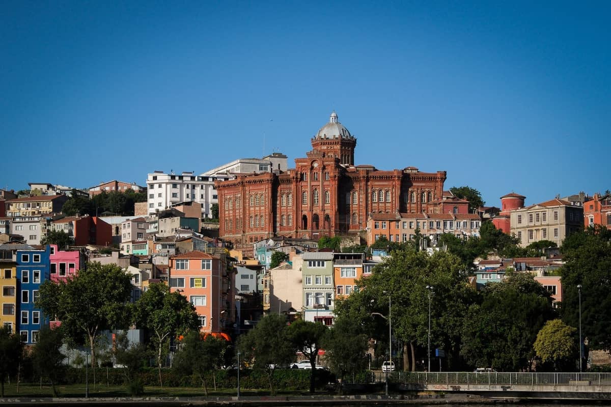 Weitwinkelansicht des berühmten Phanar Greek Orthodox College aus roten Backsteinen mit Blick auf die bunten Häuser im Viertel Fener-Balat, Istanbul, unter einem klaren blauen Himmel.