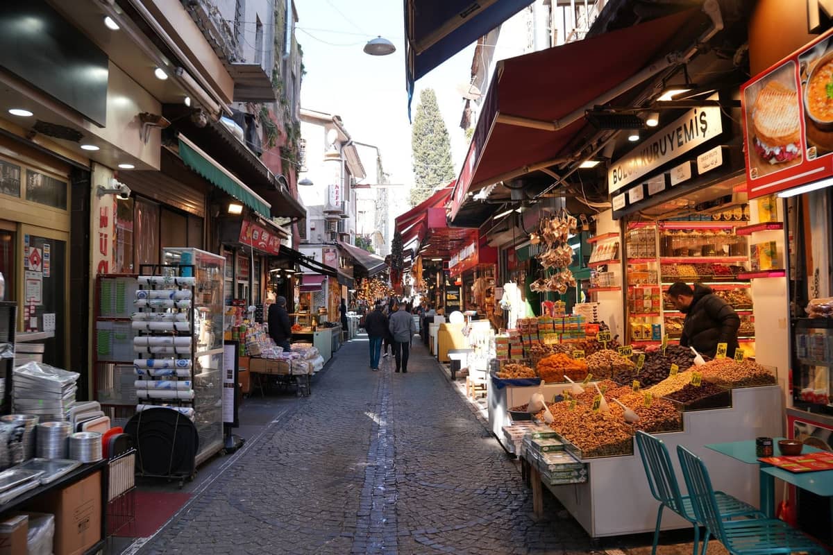 Una animada calle de mercado en Estambul repleta de tiendas de regalos, frutos secos y puestos de especias bajo toldos con gente de compras.