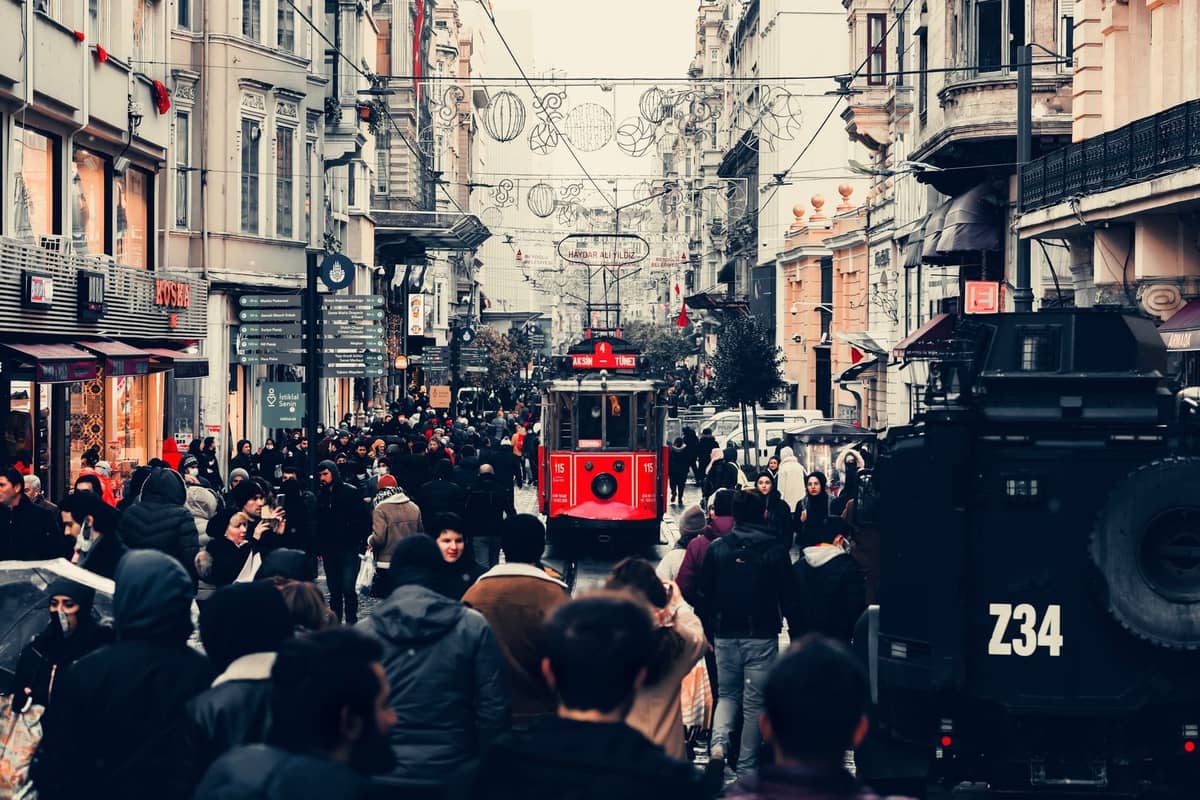 Concurrida calle İstiklal Caddesi en Estambul con multitudes, tiendas y el icónico tranvía rojo en el centro.