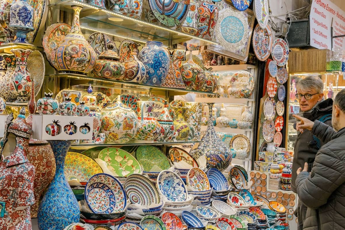 Puesto colorido en Estambul que vende cerámica tradicional de estilo Iznik, cuencos, platos y jarrones con patrones intrincados y dos personas comprando.