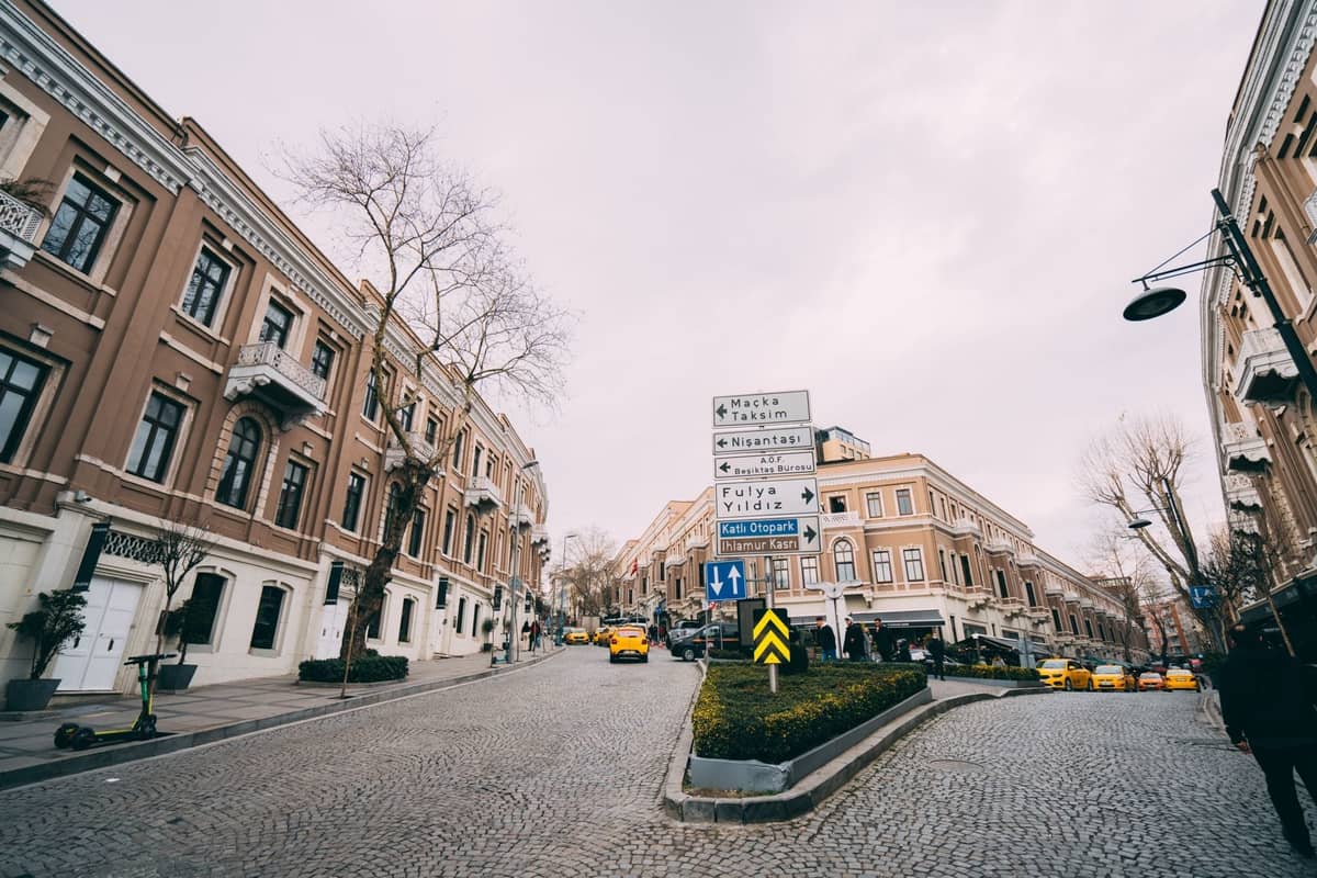 Una calle amplia y tranquila en el barrio de Nişantaşı de Estambul, flanqueada por elegantes edificios, tiendas de lujo y taxis amarillos bajo un cielo nublado.