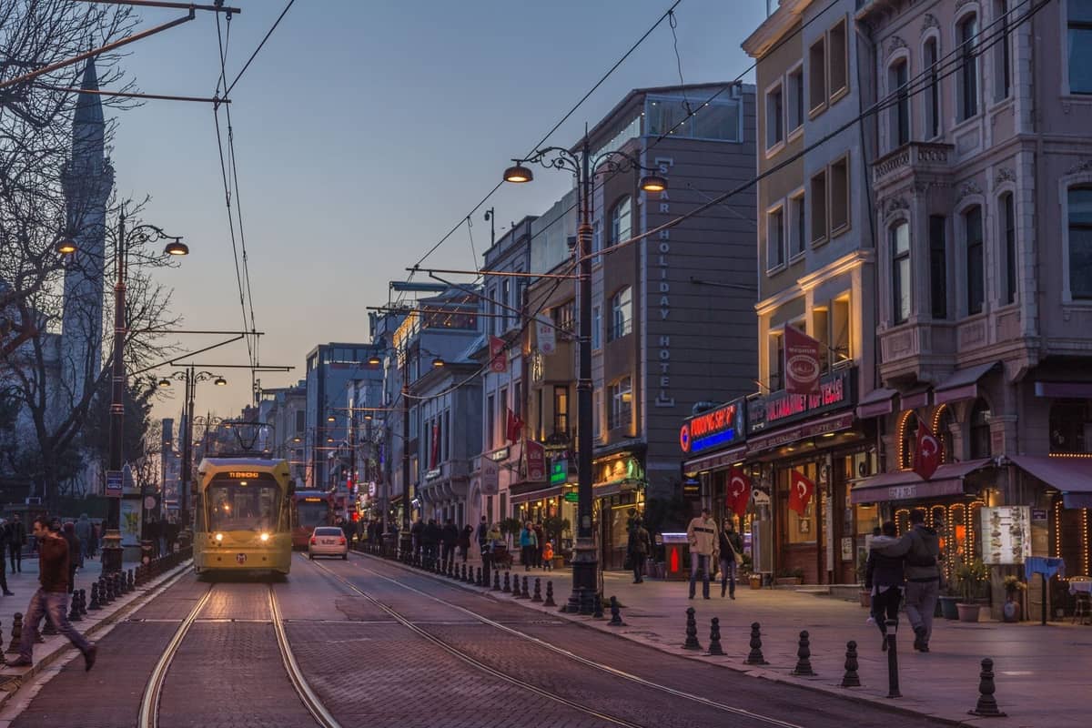 Belebte Straße in Istanbul mit Straßenbahn, Fußgängern, Geschäften und Abendlichtern in einem lebhaften Stadtviertel.