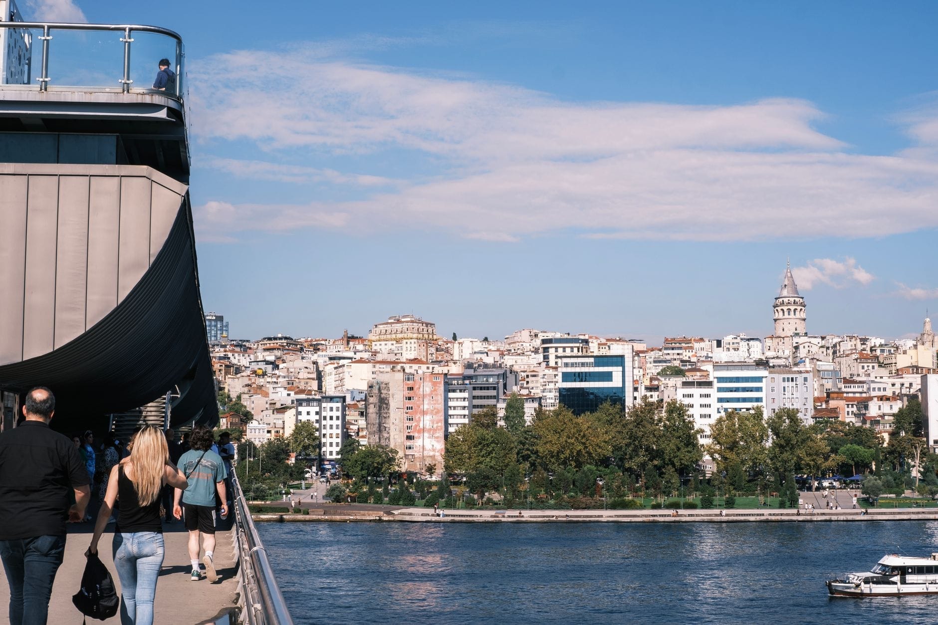 Pessoas caminhando em uma ponte sobre a água com o skyline de Istambul e a Torre Gálata ao fundo em um dia ensolarado.