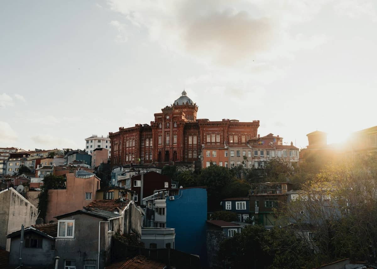 Stadtpanorama von Istanbul bei Sonnenuntergang mit dem markanten roten Backsteingebäude des Fener Greek Orthodox College auf einem Hügel, umgeben von Gebäuden des umliegenden Viertels.