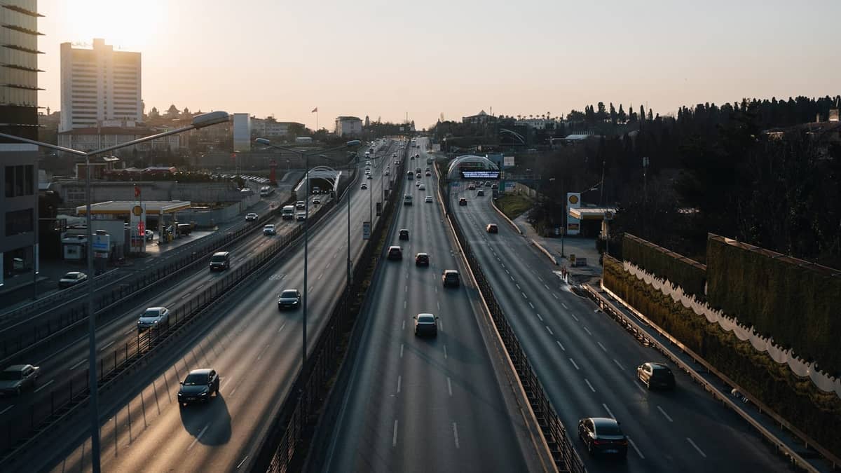 Breite Autobahn in Istanbul mit mehreren fahrenden Autos, modernen Gebäuden im Hintergrund und abendlichem Sonnenlicht.
