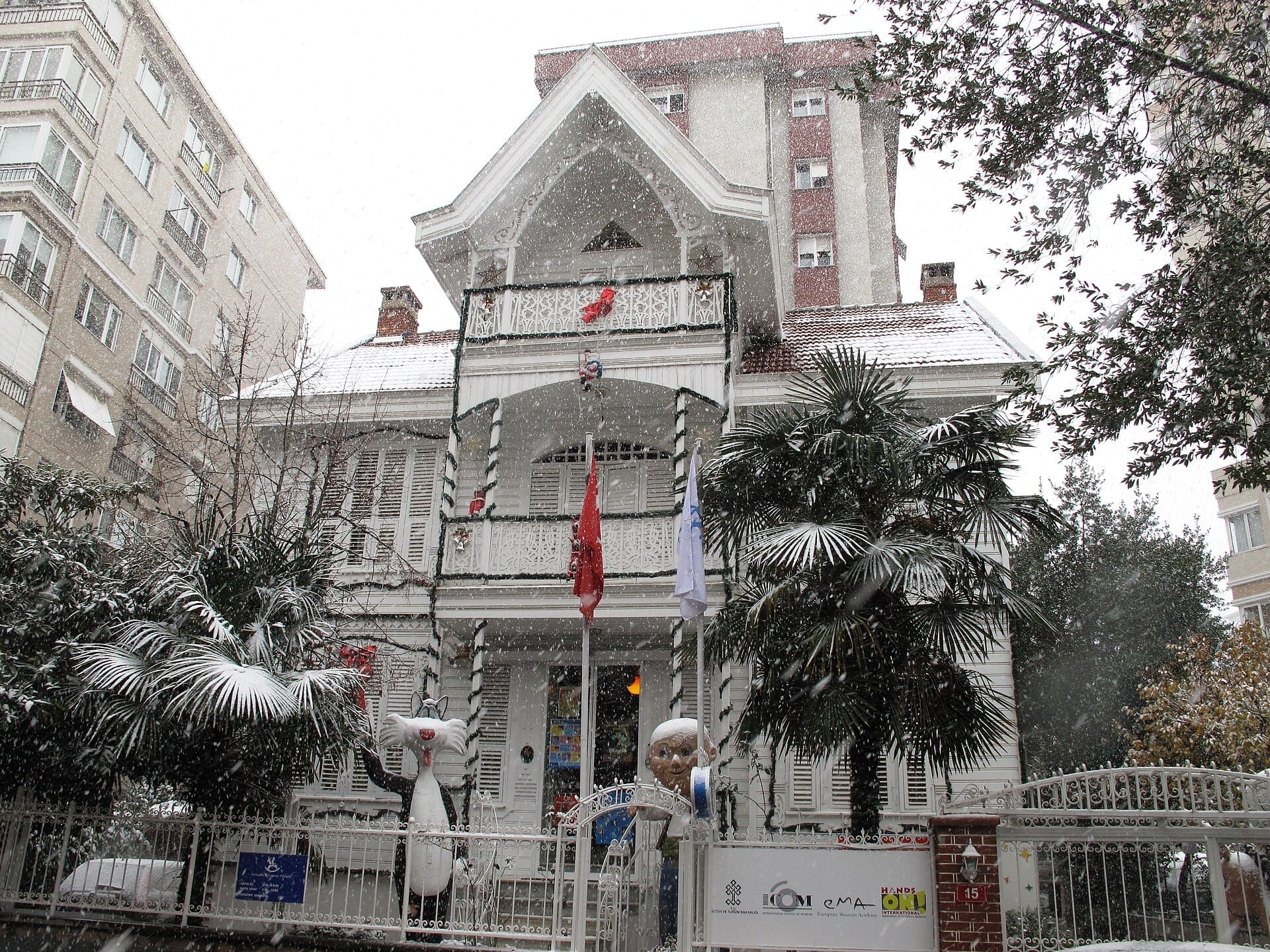 Storica villa in legno che ospita l'Istanbul Toy Museum a Kadıköy, circondata da palme innevate e bizzarre statue di giocattoli all'ingresso.