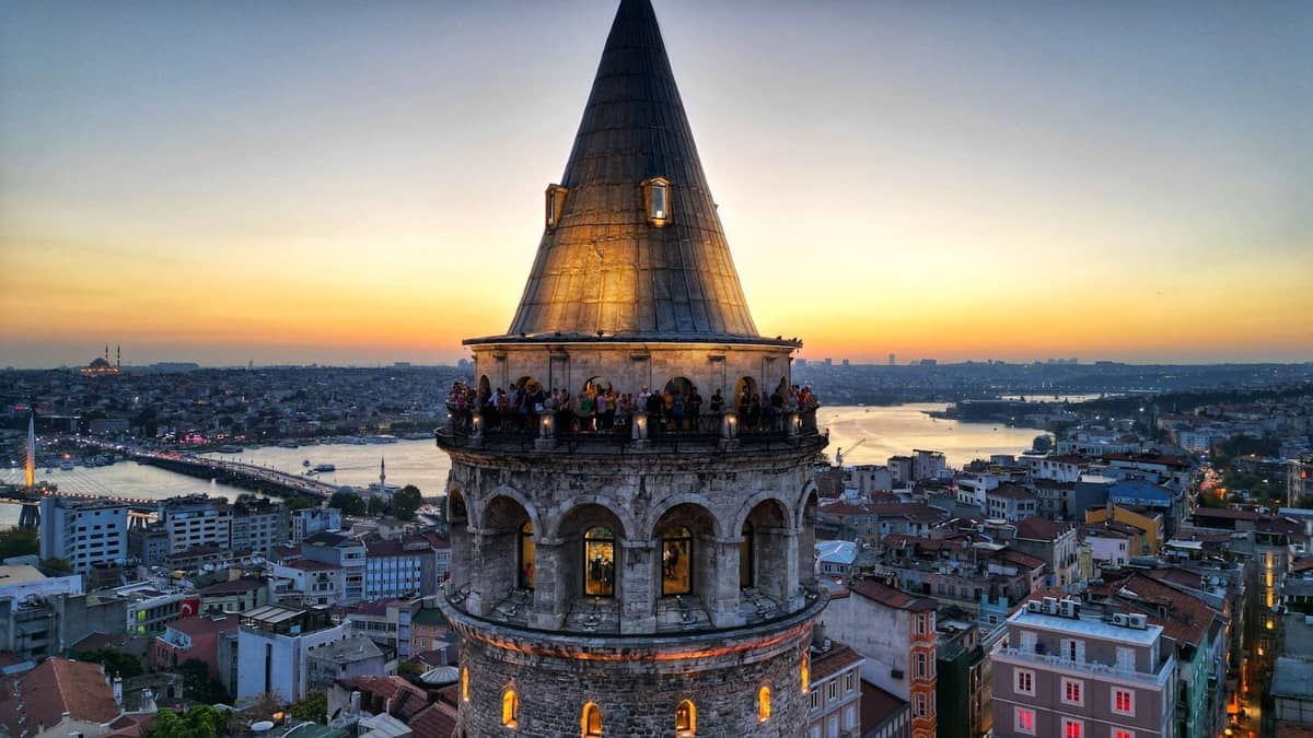 Nahaufnahme des beleuchteten Galata-Turms bei Sonnenuntergang mit Panoramablick auf Istanbul und den Bosporus im Hintergrund.