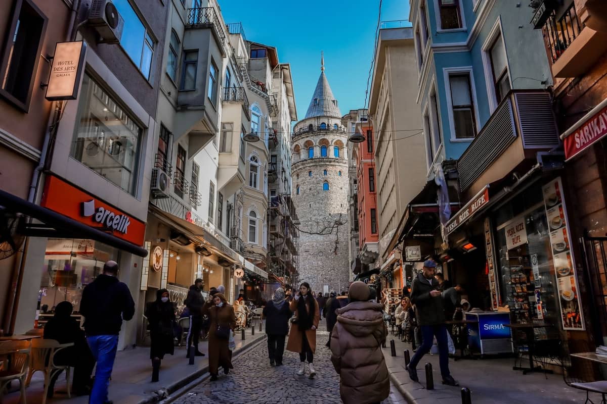 Widok wzdłuż tętniącej życiem ulicy w kierunku Wieży Galata, otoczonej kolorowymi budynkami i spacerującymi ludźmi, symbolizującej serce Beyoğlu i Galaty.
