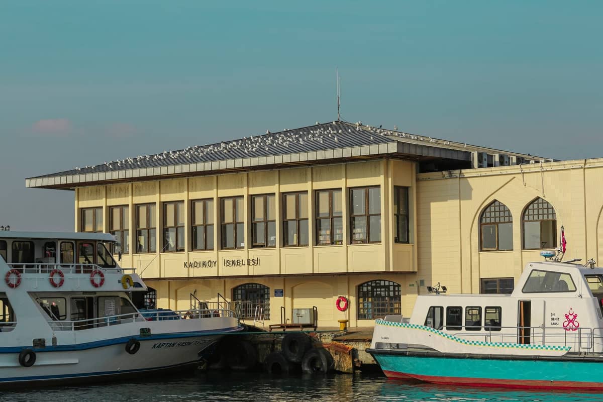 Terminal promowy Kadıköy po azjatyckiej stronie Stambułu z zacumowanymi promami i mewami na dachu, pod bezchmurnym błękitnym niebem.