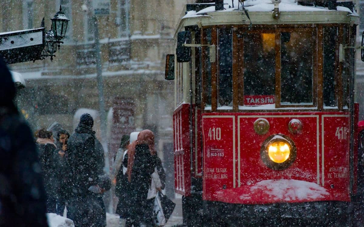 O histórico bonde vermelho de Istambul avança pela neve com pessoas agasalhadas e flocos caindo no centro da cidade, contestando o mito do calor perpétuo.
