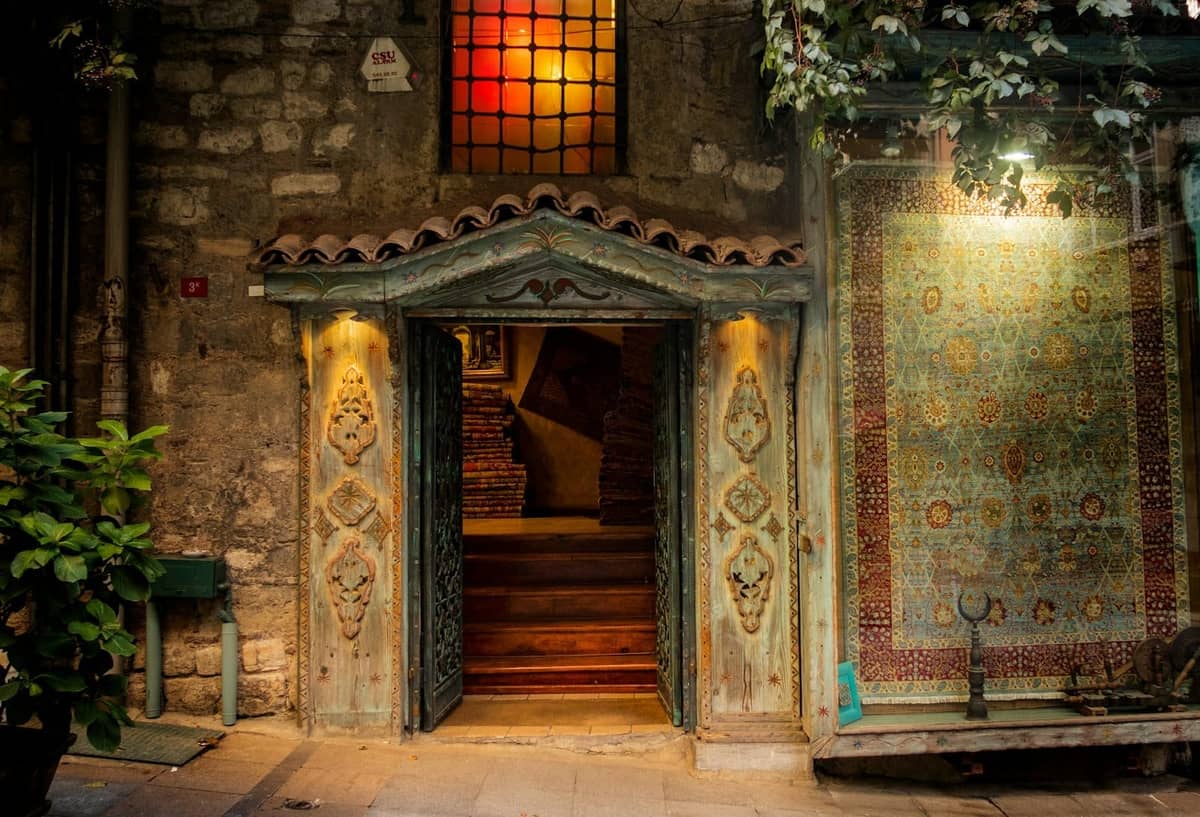 Un ingresso in pietra dall'illuminazione calda con dettagli architettonici storici a Istanbul, accanto a un'esposizione di tappeti tradizionali.
