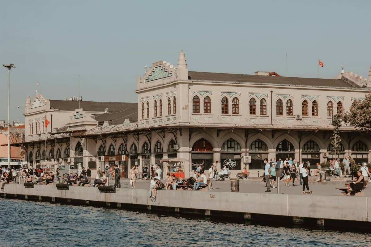 Vista sul lungomare della stazione ferroviaria di Sirkeci a Istanbul con persone che camminano e siedono vicino all'edificio del terminal.