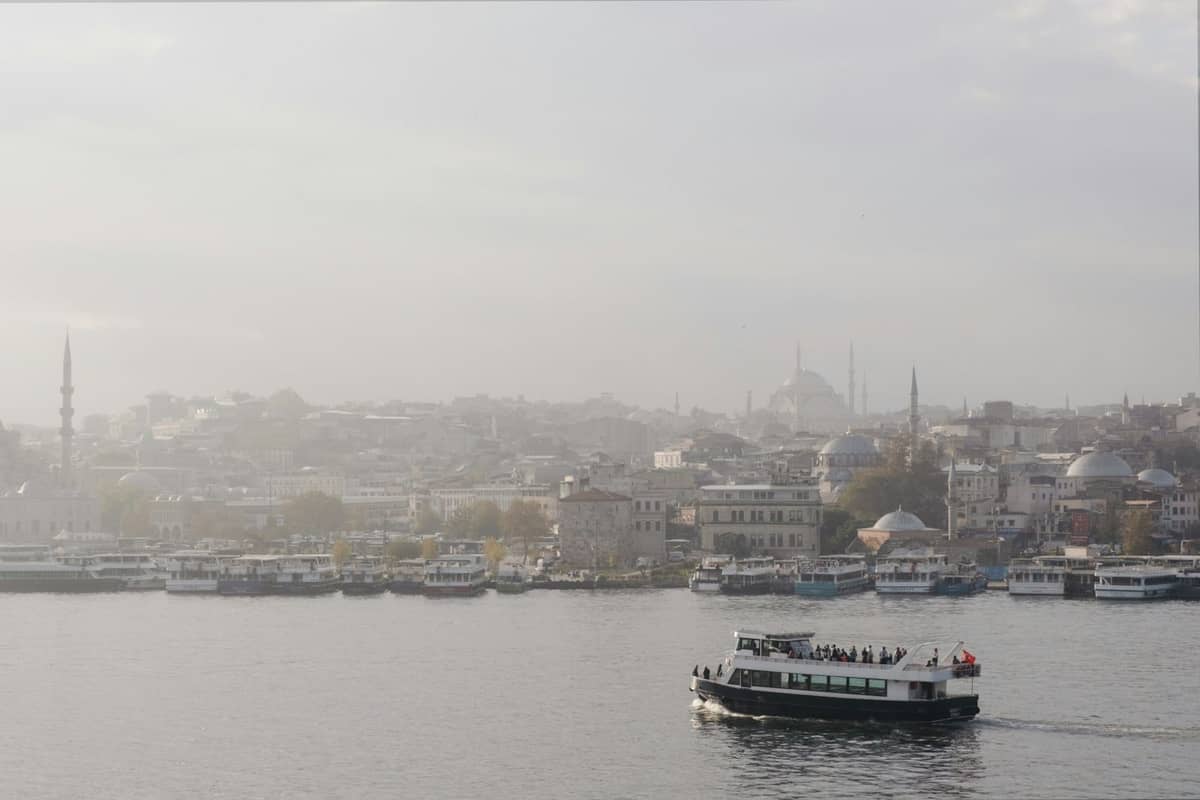 Eine Pendlerfähre überquert den Bosporus mit der Skyline von Istanbul, Moscheen und Kuppeln im Hintergrund bei sanftem Tageslicht.