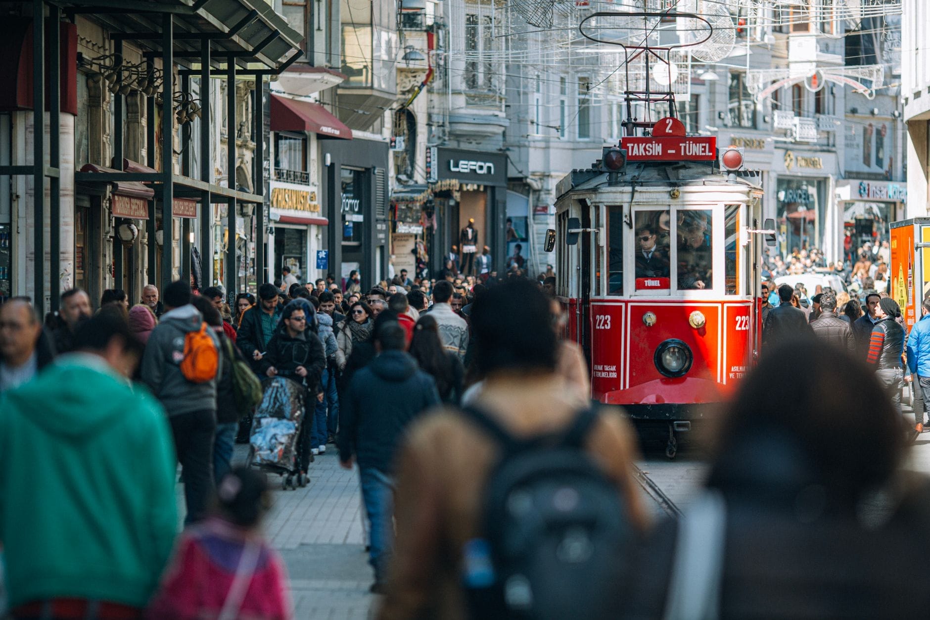 Viale İstiklal affollato con il leggendario tram rosso nostalgico che avanza tra i pedoni, circondato da edifici storici e dalla vivace vita di strada di Istanbul.