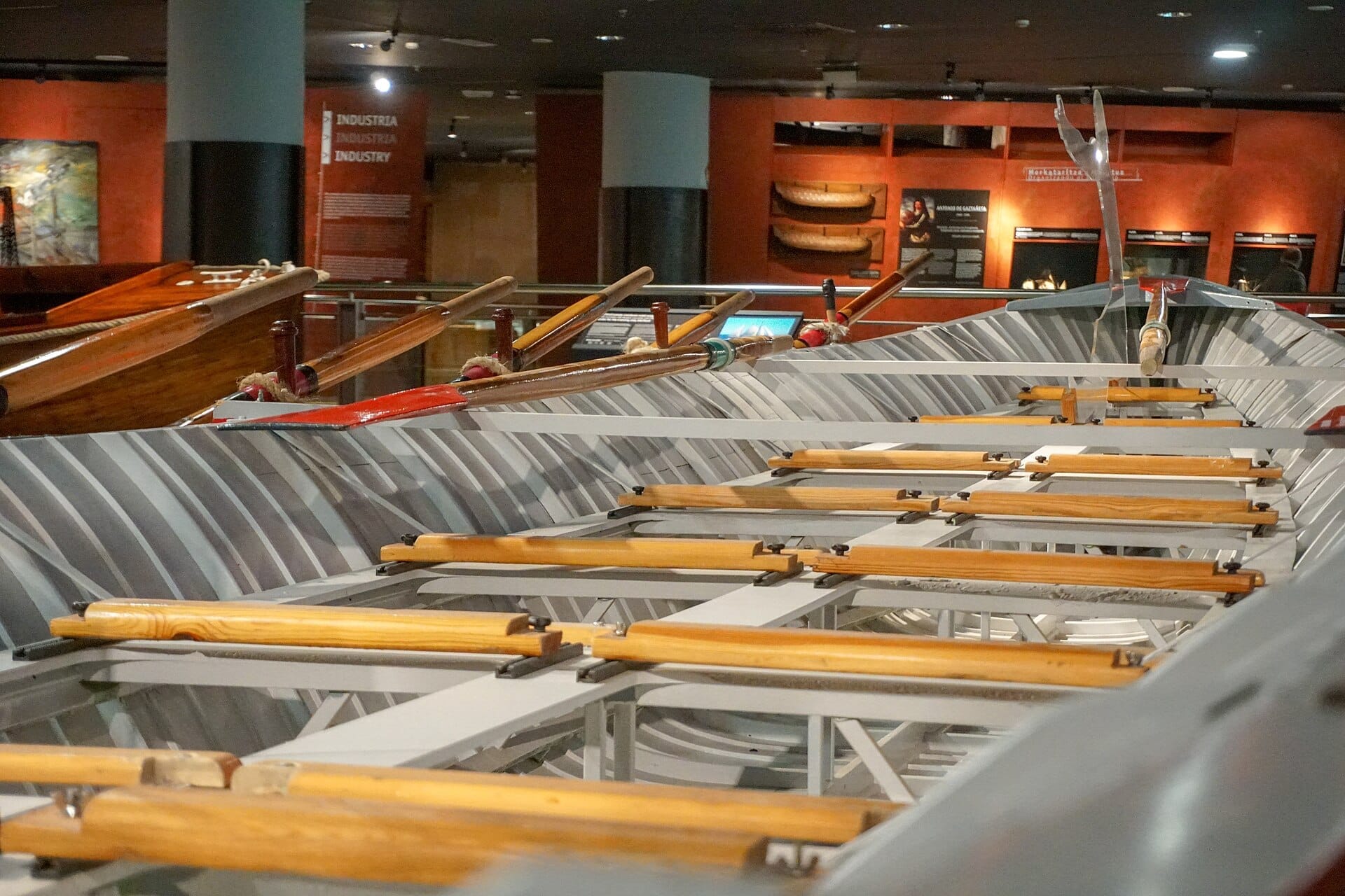 Close-up of wooden oars lined in a traditional rowing boat, displayed indoors at Itsasmuseum Bilbao's maritime exhibit.