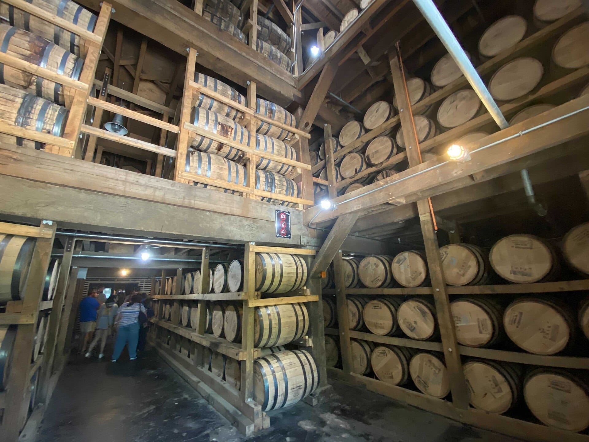 Vista interior del almacén de barriles de la destilería Jack Daniel's, con filas de barriles de whiskey apilados y un grupo de visitantes en un recorrido.