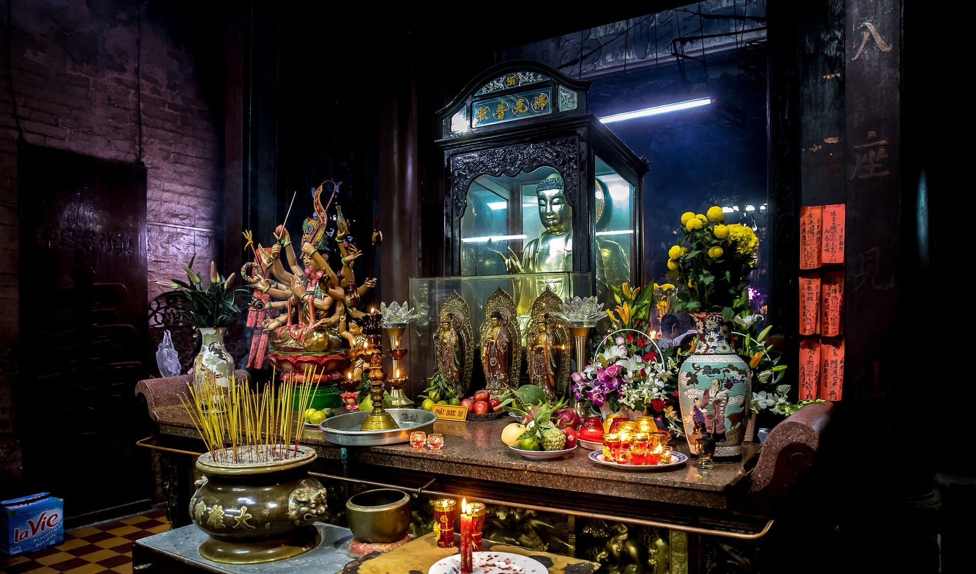 Altar ornamentado dentro de la Pagoda del Emperador de Jade con estatua dorada de Buda, varillas de incienso, ofrendas de frutas, flores y vibrantes figuras religiosas.