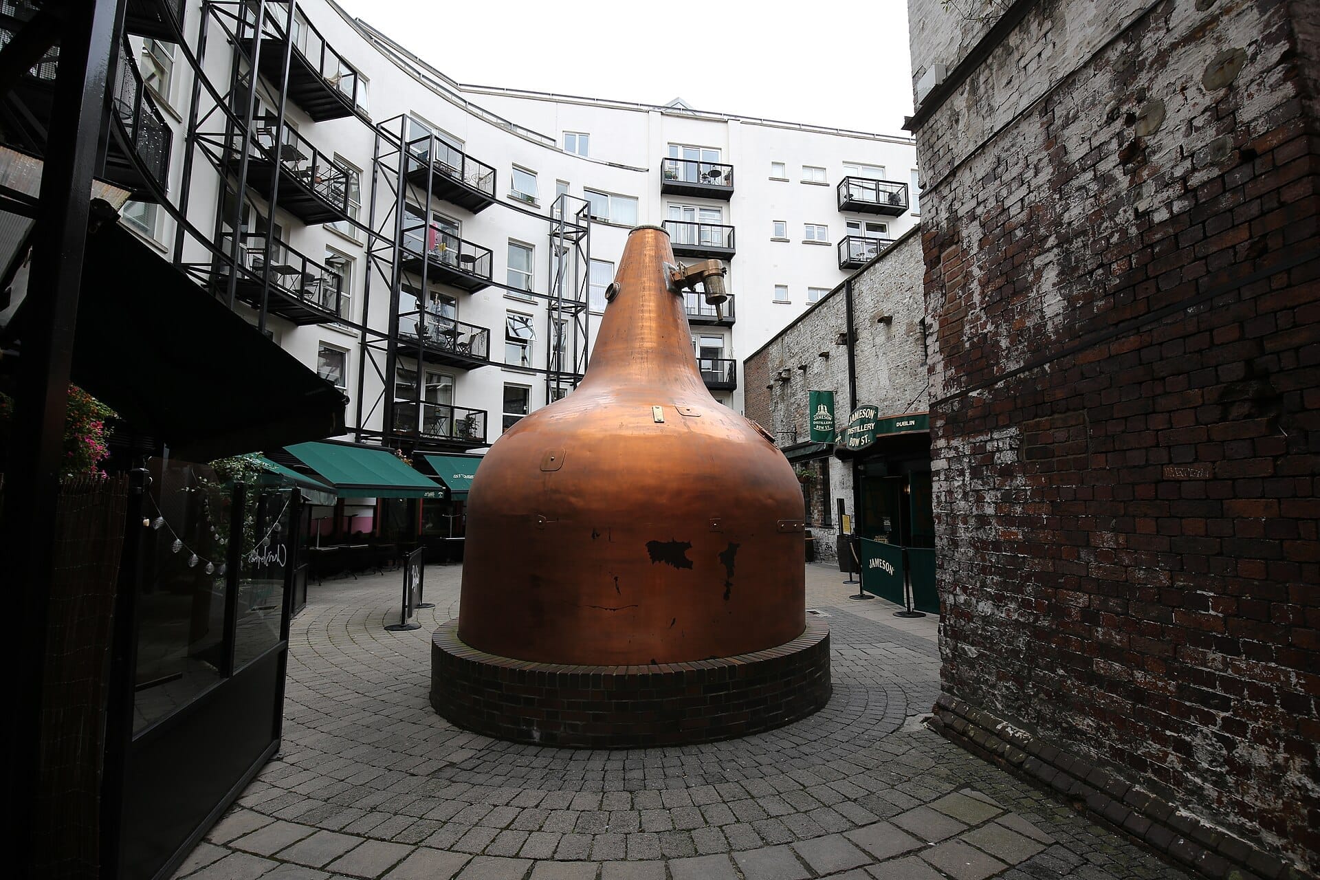 Grande alambicco in rame all'esterno della Jameson Distillery Bow St, circondato da muratura storica e appartamenti moderni nel quartiere Smithfield di Dublino.