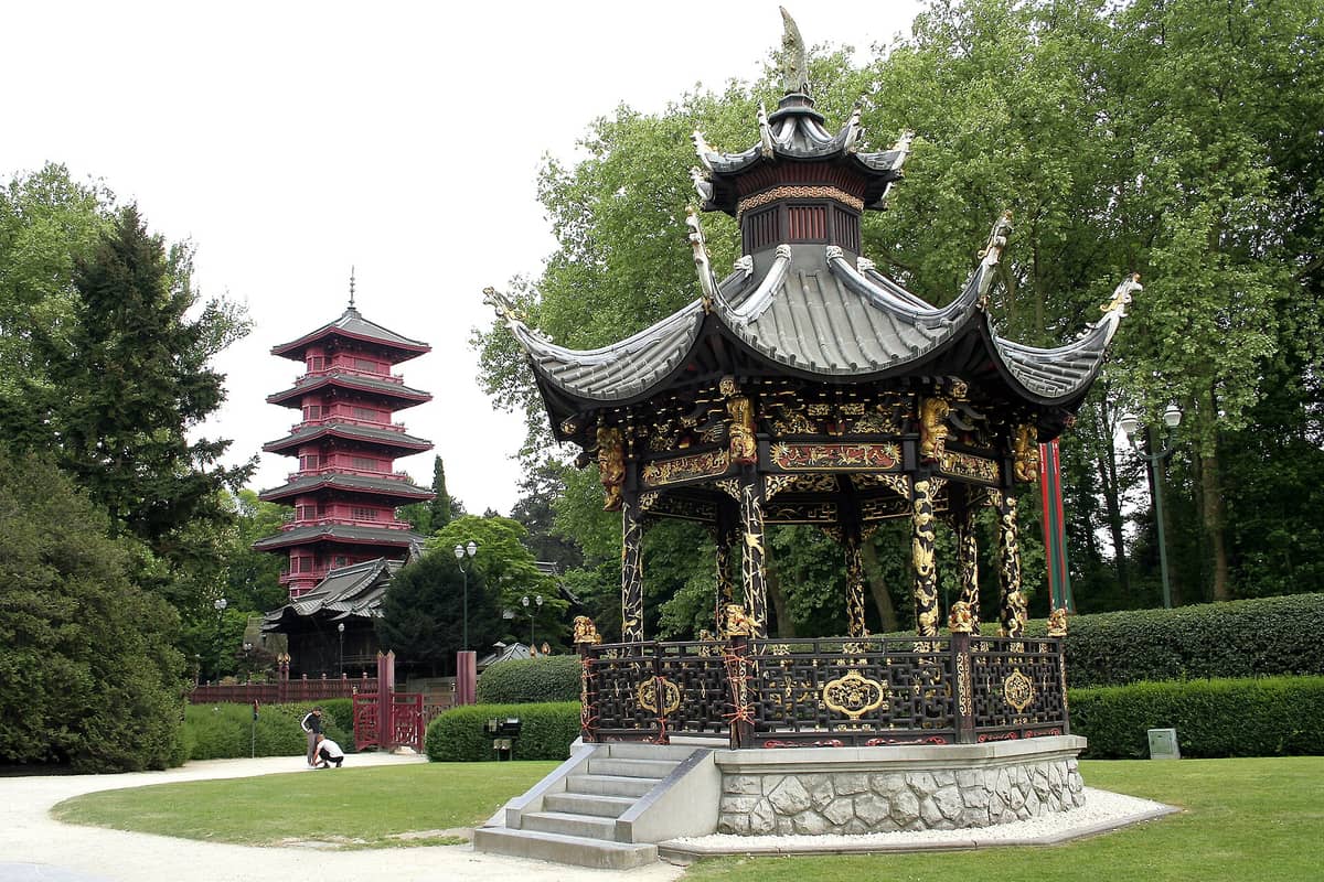A Torre Japonesa e o ornamentado Pavilhão Chinês no domínio de Laeken, em Bruxelas, cercados por árvores e jardins, com a pagode vermelha em destaque ao fundo.