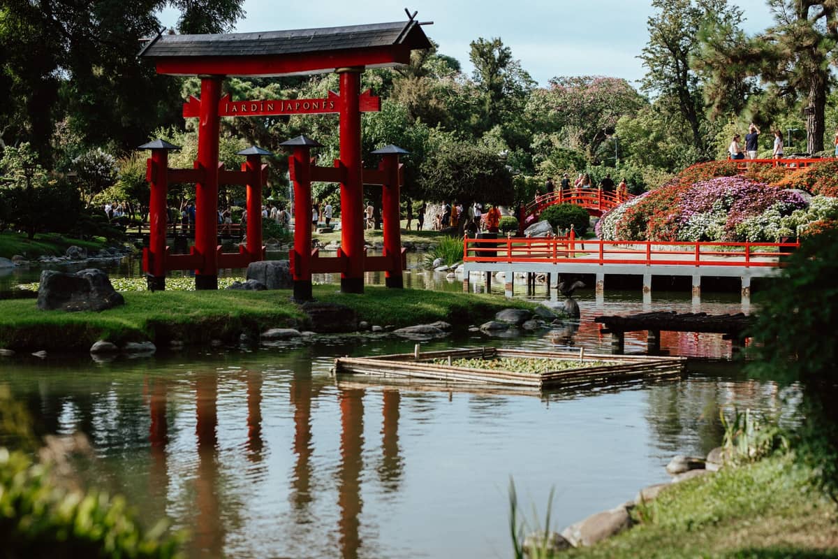 มุมกว้างของ Jardín Japonés ในบัวโนสไอเรส เห็นเสาโทริอิ สะพานแดง สระน้ำ และสวนภูมิทัศน์สีเขียวสดใสในวันแดดออก